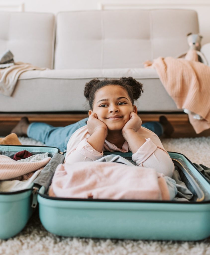 A child lying down on a half packed suitcase