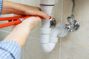 Plumber fixing a pipe under the sink with an orange wrench