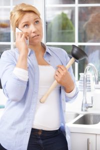 A lady holding a toilet plunger while standing in front of the kitchen sink