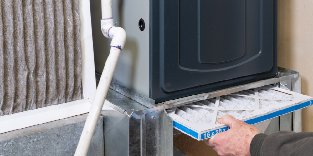 Person replacing an HVAC filter in their furnace to prepare for winter - Common Winter HVAC Issues and How to Prevent Them - Black Diamond Plumbing & Mechanical
